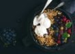 Oat granola crumble with fresh berries, seeds and ice-cream in iron skillet pan on dark wooden board over black backdrop