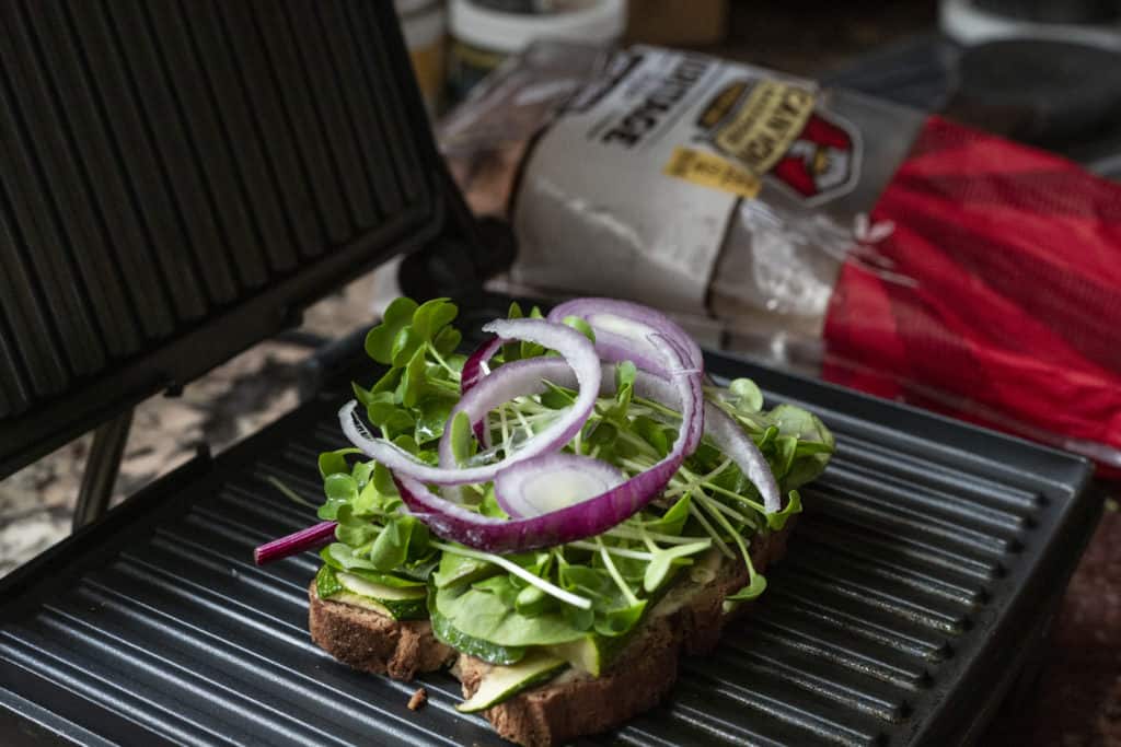 slice of bread on top of dark grill with greens and onion on top with bread back in background