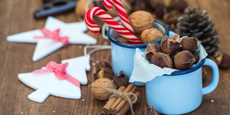 Traditional Christmas foods and decoration. Roasted chestnuts in blue enamel mug, walnuts, cinnamon sticks, candy canes, pine cone on rustic wooden background