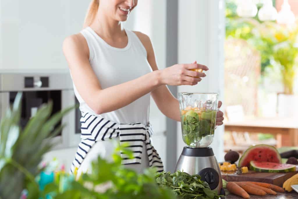 Happy vegan woman mixing a healthy smoothie with green vegetables