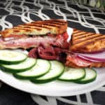 grilled sandwich with lunchmeat with cucumber slices and olives on a graphic background