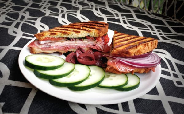 grilled sandwich with lunchmeat with cucumber slices and olives on a graphic background