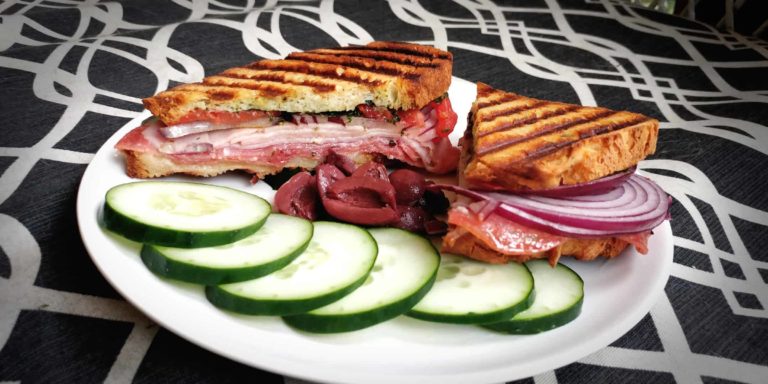 grilled sandwich with lunchmeat with cucumber slices and olives on a graphic background