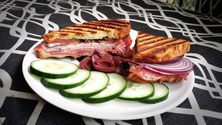 grilled sandwich with lunchmeat with cucumber slices and olives on a graphic background
