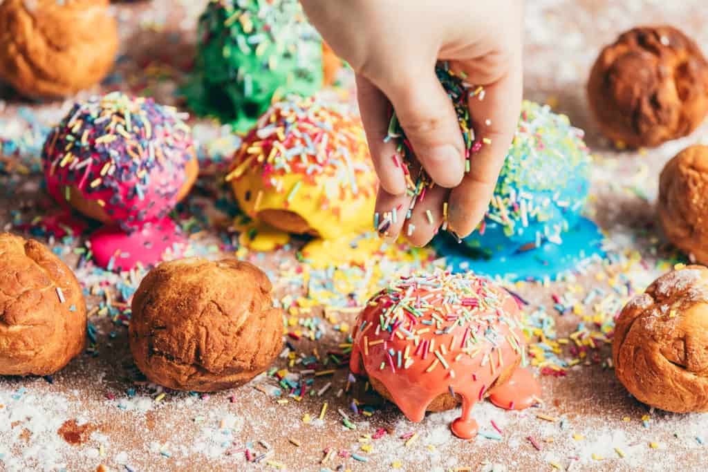 Woman's hand sprinkling sugar sprinkles on colorful donuts. Decoration process.
