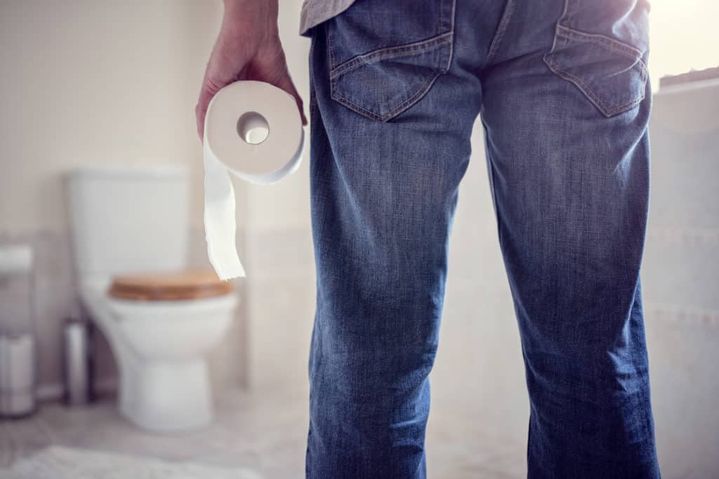 Man holding toilet tissue roll in bathroom looking at toilet