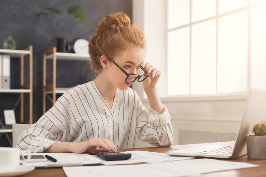 Financier woman in glasses working on laptop and counting financial accounts in office. Concentrated female manager working on marketing strategy at workplace