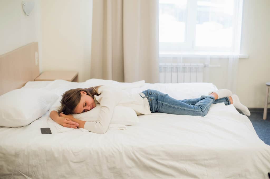 A woman laying on her bed still dressed in her clothes to tired to get in the bed.