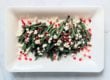 roasted green beans with crumbled goat cheese and pomegranate seeds on a white rectangular plate and light grey background