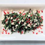roasted green beans with crumbled goat cheese and pomegranate seeds on a white rectangular plate and light grey background