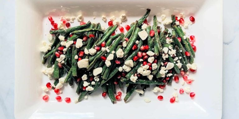roasted green beans with crumbled goat cheese and pomegranate seeds on a white rectangular plate and light grey background